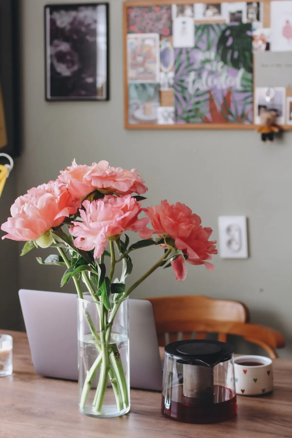 Coral peonies in a glass vase beside a pot of tea