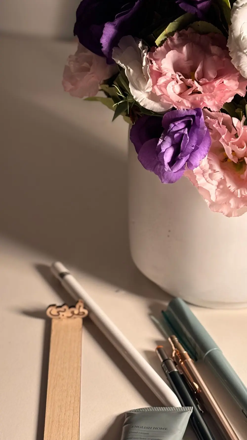 Pink, white and purple flowers in soft light beside pens and a bookmark